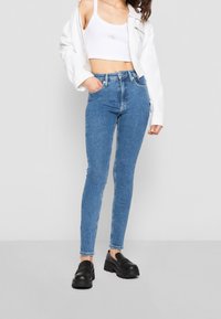 Smal jeans i ljusblå denim, hög midja, med fem fickor och bältesöglor. Matchas med en vit kort rakad topp och en vit jacka.