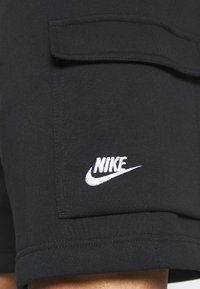 Svarta shorts i mjukt tyg, med en framficka och broderad vit Nike-logga på det nedre benet. Enkel design och textur.