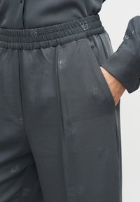 Σκούρο γκρι παντελόνι με ελαστική μέση, διαθέτοντας διακριτικό ανάγλυφο μοτίβο με το λογότυπο "HUGO" και πλαϊνές τσέπες. Ομαλή υφή υφάσματος.