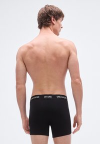 Black cotton boxer briefs with a text-logo waistband, snug fit, and mid-rise design, viewed from the back on a neutral background.