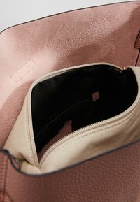 Sac en cuir marron avec une pochette zippée en tissu beige ouverte à l'intérieur, montrant une doublure intérieure noire et une petite poche intérieure zippée.