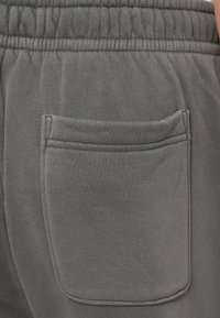 Sive trenirke z v textured bombažno tkanino, elastičnim pasom in eno zadnjo žepom s šitimi detajli.