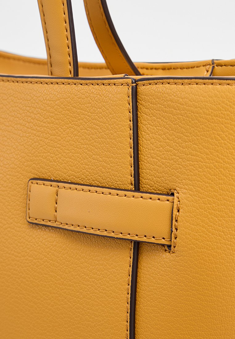 Sac fourre-tout en cuir jaune avec une surface texturée, des coutures brunes contrastantes et un détail de sangle horizontale sur le devant.