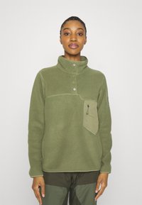 Olivgrüner Fleece-Pullover mit hohem Kragen, drei Knöpfen, einer mit Reißverschluss versehenen Brusttasche und kontrastierendem, hellerem Tascheneinsatz.