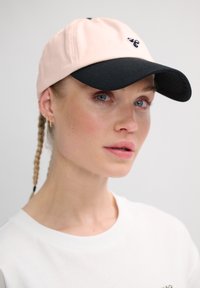 Pink cotton cap with a black visor, featuring a small embroidered logo on the front and a textured underside of the visor.