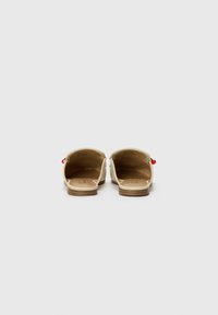 Zapatos beige de tacón abierto con textura suave, tacones de madera y pequeños acentos decorativos rojos y verdes en los laterales.