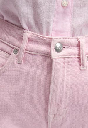 Nærbilde av rosa denimjeans med sølvfarget Lee-knapp og en lyserosa skjorte stukket inn.