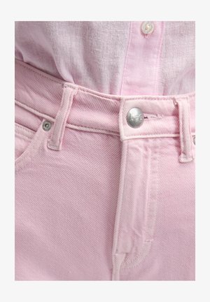 Nærbilde av rosa denimjeans med sølvfarget Lee-knapp og en lyserosa skjorte stukket inn.