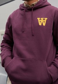 Vínová mikina s kapucí z bavlněné směsové látky s žlutě vyšívaným písmenem "W" na hrudi a přední kapsou.
