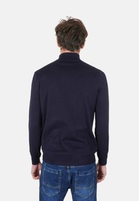 Maglione aderente blu navy con collo alto e polsini e orlo a coste, abbinato a jeans in denim blu. Tessuto semplice e liscio a maglia.