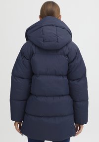 Námořnická pufovaná bunda s kapucí, která má prošívaný design, oversized střih a elastické manžety. Hladká textura a délka po střední stehna.