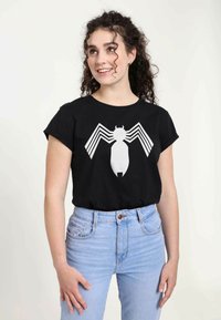 Sort bomulds-t-shirt med et stort hvidt edderkoppemotiv og stribede accenter. Kombineret med højtaljede lyse blå jeans.