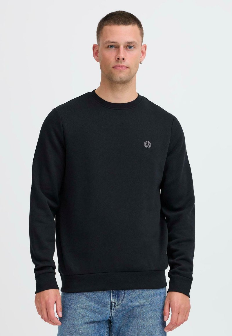 Sudadera negra con cuello redondo y mangas largas, que presenta un pequeño logo en el lado izquierdo del pecho. Tejido suave y puños con ribete.