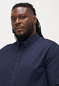 Camicia azzurra navy con colletto rigido, dotata di una superficie liscia e di una pattina frontale con bottoni coordinati.