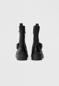 Black leather ankle boots with a rounded toe, side zippers, and textured rubber sole. Features a loop accent on the side.