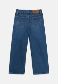 Denim jeans in medium blue, featuring a straight leg cut, two back pockets, and a tan leather waistband tag with brand logo.