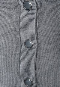 Szary sweter z dzianiny z pionowym prążkowaniem i dużymi, czarnymi plastikowymi guzikami z przodu. Gładka faktura i dopasowany krój.