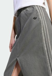 Grå denimskjørt med elastisk liv, sidespalte og tre kontraststriper nedover siden. Har en liten svart logoaccent.