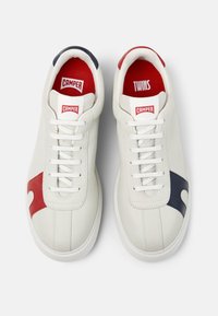 Un paio di sneakers bianche Camper con accenti rossi e blu navy, fodera interna rossa e la dicitura "CAMPER" e "TWINS" stampata nelle sole interne.