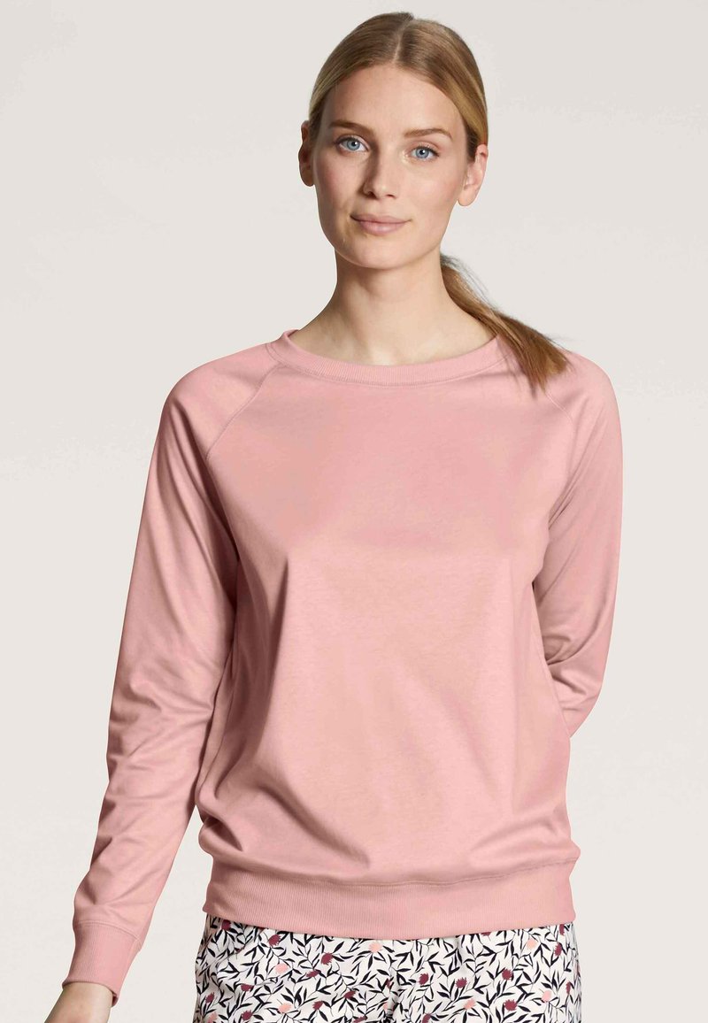 Light pink sweatshirt with long raglan sleeves and a ribbed neckline. Soft texture, paired with patterned bottoms featuring floral designs.