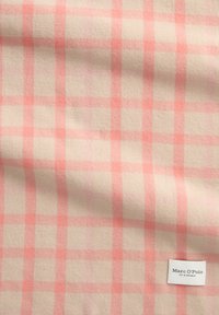 Tissu doux avec un motif à carreaux beige et rose, comportant une petite étiquette blanche indiquant "Marc O’Polo EST. À STOCKHOLM" dans le coin inférieur droit.