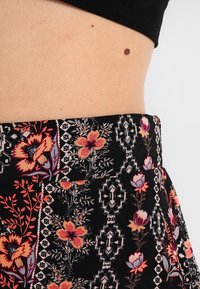 Falda de tela negra con un diseño floral en tonos rojo, naranja y azul. La cinturilla es plana y tiene una sutil textura con un patrón.