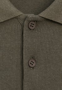 Gros plan sur un tissu tricoté côtelé vert olive avec deux boutons brun foncé à quatre trous et un col plié.