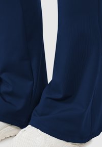 Pantaloni sportivi blu navy realizzati in materiale liscio e elastico, con taglio dritto e dettagli di cucitura discreti, abbinati a sneakers bianche.