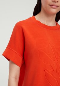 Korte mouwen feloranje sweatshirt van zacht materiaal met een reliëf bloemenontwerp aan de voorkant, featuring een ronde halslijn en gestikte randen.