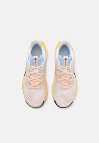 Baskets de course rose clair avec une tige en mesh, détails jaunes, intérieur bleu et semelle extérieure texturée ; elles présentent des lacets fins et des accents de logo.
