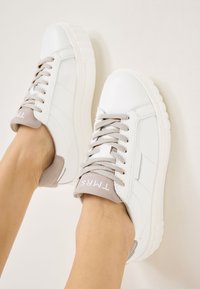 Baskets en cuir blanc avec un talon en daim gris, lacets texturés, bout rond et une épaisse semelle en caoutchouc blanc. Logo sur l'étiquette du talon.