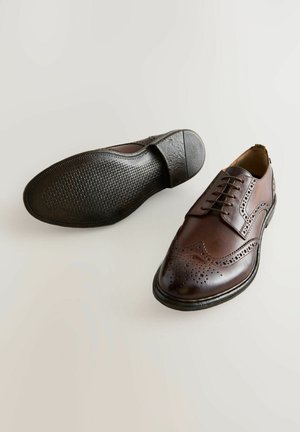 Smeđe kožne cipele za odijelo s dizajnom krila, detaljima broguea, vezicama i teksturiranom gumenom potplatom. Klasičan i elegantan oblik.