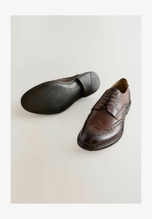 Smeđe kožne cipele za odijelo s dizajnom krila, detaljima broguea, vezicama i teksturiranom gumenom potplatom. Klasičan i elegantan oblik.