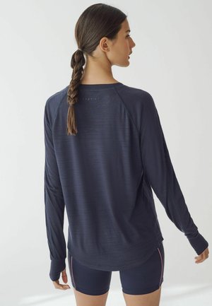 Navyblaues langärmliges Sporthemd mit strukturierter Oberfläche, Raglanärmeln und abgerundetem Saum, kombiniert mit eng anliegenden navyblauen Shorts mit pinkfarbenen Akzenten.