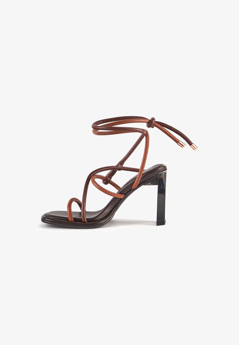Sandale à talon haut avec semelle noire et plusieurs fines lanières en cuir marron enroulées autour du pied et de la cheville, avec un talon bloc.