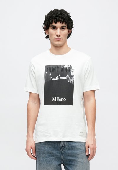 Biele bavlnené tričko s čiernobielou grafickou potlačou s nápismi „Emporio Armani“ a „Milano“. Okrúhly výstrih, krátke rukávy.