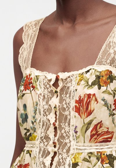 Gros plan d'une robe fleurie avec bordure en dentelle et boutons recouverts de tissu sur les épaules et le devant, portée par une personne à la peau foncée.