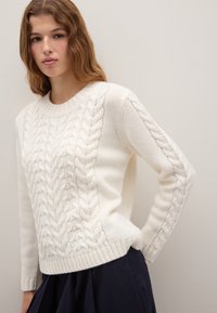 Cream cable-knit sweater with a round neck and ribbed cuffs, featuring textured patterns along the sleeves and body.