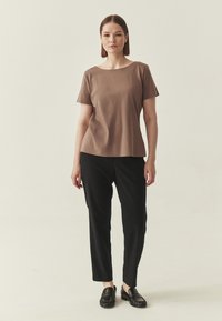 Haut marron à manches courtes avec une coupe décontractée, associé à un pantalon noir slim et des mocassins noirs, sur un fond neutre.