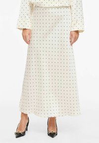 Jupe longue couleur crème à pois noirs, en tissu lisse. Accentuée d'un léger éclat et associée à des talons noirs pointus.