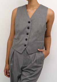 Grau gestreifter Weste mit V-Ausschnitt, sechs schwarzen Knöpfen und zwei seitlichen Taschen. Getragen über einer hochtaillierten Hose mit Bundfalten.