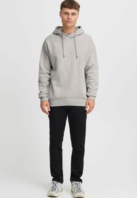 Haut à capuche gris avec une poche kangourou à l'avant, un cordon de serrage à la capuche et des poignets côtelés, associé à un jean noir et des baskets multicolores.
