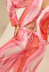 Rosa und orangefarbene transparente Loungewear-Set mit einem lockeren Oberteil mit Bändchen und einer Hose mit elastischem Bund und dekorativen Perlen.