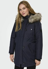 Námornícky modrý parka s kapucňou podšitou umelou kožušinou, s gombíkovým a zipsovým zapínaním, dvoma bočnými vreckami a elastickým pásom.
