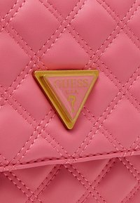 Sac à main matelassé rose en matériau synthétique, avec un logo triangulaire doré proéminent sur un fond rose et des détails de couture.