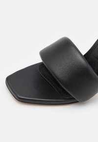 Gros plan d'une sandale en cuir noir avec un bout carré et une large bride rembourrée à l'avant.