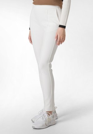 Pantaloni bianchi aderenti con un design pulito, caratterizzati da pieghe laterali e una texture liscia, abbinati a scarpe da ginnastica bianche.