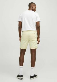 Shorts jaune clair avec ourlets roulés, poches arrière et un petit logo. Associés à un t-shirt blanc uni et des baskets noires.