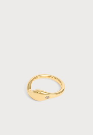 Guld farvet ring med en lille rund diamant sat på en glat buet bånd mod en lys grå baggrund.