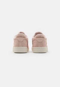 Zapatillas Reebok en suave ante rosa claro con forro de piel blanca y suela de goma texturizada de color blanco roto; cuenta con el logo grabado en la parte posterior.
